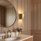 A transitional bathroom featuring a brushed brass wall sconce mounted beside a round mirror above a marble vanity with blue striped wallpaper and tan wainscoting.
