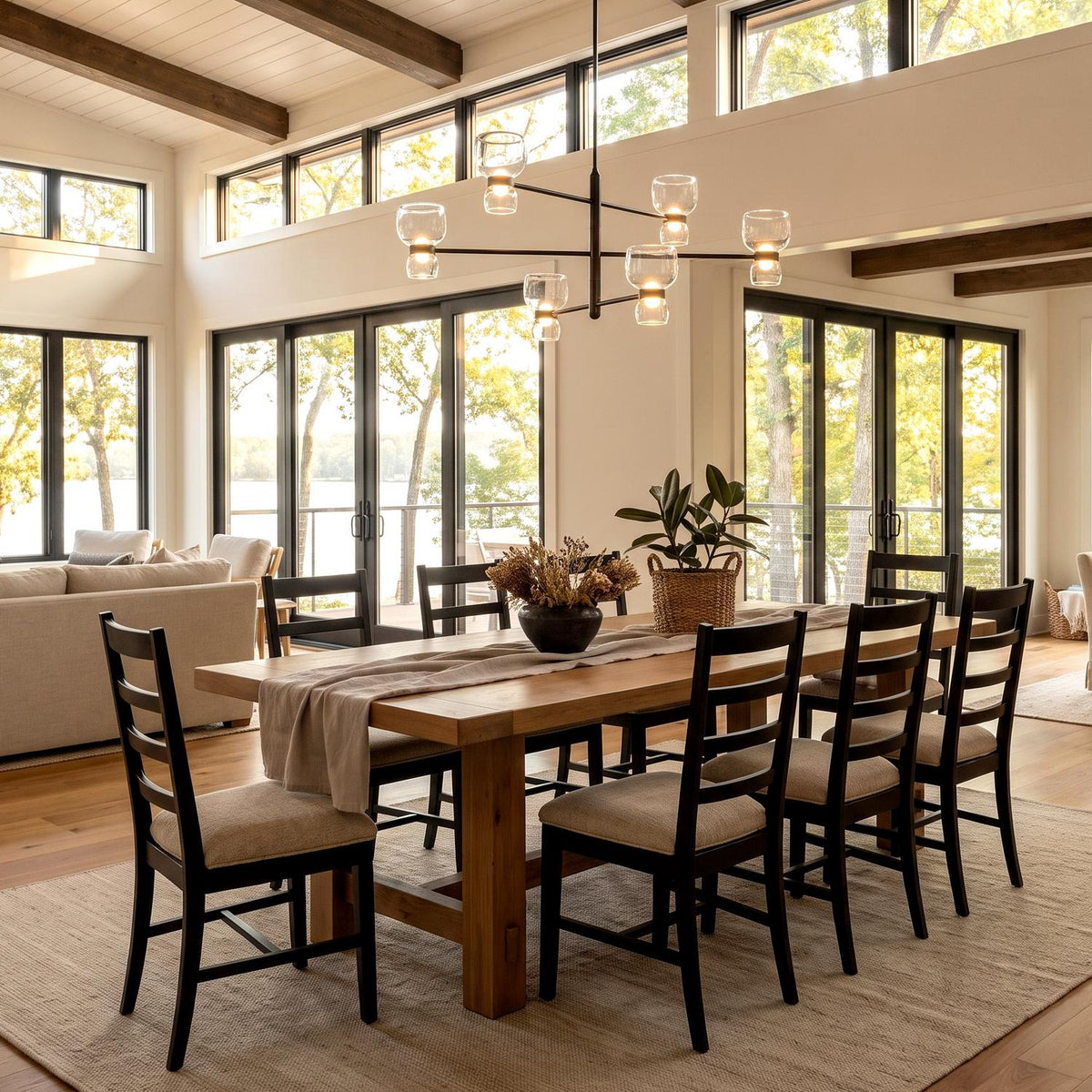A modern farmhouse dining room featuring a dark bronze chandelier with clear glass shades hanging over a light wood dining table under exposed ceiling beams.