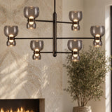 A contemporary living room featuring a Brann LED Chandelier in urban bronze with smoke glass shades suspended near a stone fireplace and potted plant.