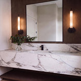 A modern bathroom with two Videl LED Wall Sconce 20", Urban Bronze fixtures in frosted glass flanking a square mirror over a marble vanity.