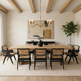 A transitional dining room featuring the Rubina 4 Light Chandelier 39", Brushed Brass over a light wood table with black cane chairs and wood beams.
