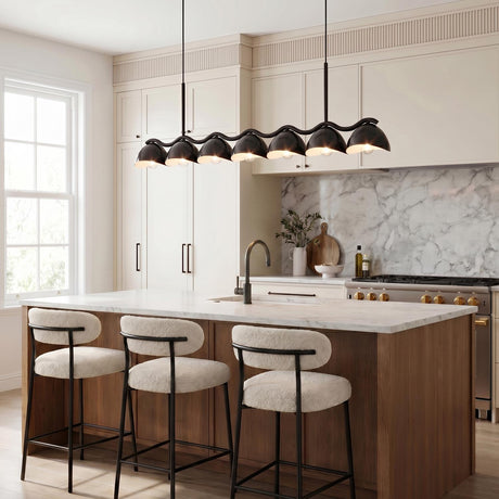 A modern kitchen featuring the Sadira 7 Light Linear Pendant 42 inch in black over a white marble island with a walnut base and three boucle stools.