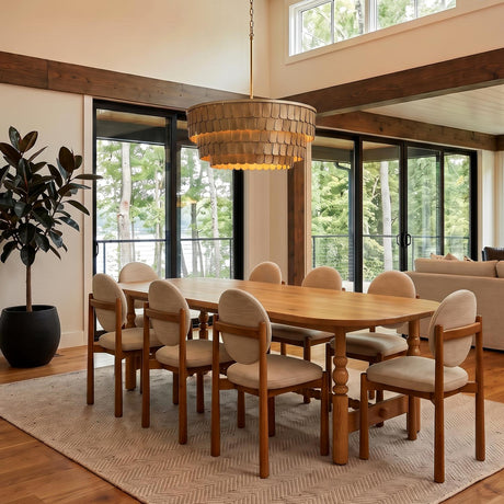 A transitional dining room with the Barina Chandelier 29", Distressed Brushed Brass hanging over a light wood table with beige chairs under dark ceiling beams.