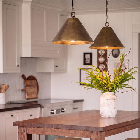 A farmhouse kitchen with two oxidized brass Kate Conical Pendants hanging over a wood island with white shaker cabinets and a shiplap ceiling.