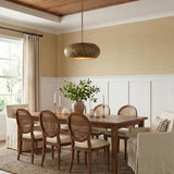 A transitional dining room with the Benicio Pendant in Burnished Patina Brass hanging over a wood table surrounded by rattan chairs and neutral grasscloth wallpaper.