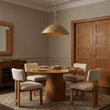 A transitional dining room with a Blaise LED Pendant in feathered brass over a round walnut dining table and four cream boucle chairs on a neutral rug.