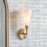 A contemporary bathroom featuring an Avani Wall Sconce 14", Matte Brass and Opal Glass mounted beside a gold arched mirror against blue and white patterned wallpaper.