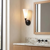 A transitional bathroom with the Avani Wall Sconce 14", Matte Black and Opal Glass mounted beside an oak-framed mirror above a white marble vanity countertop.