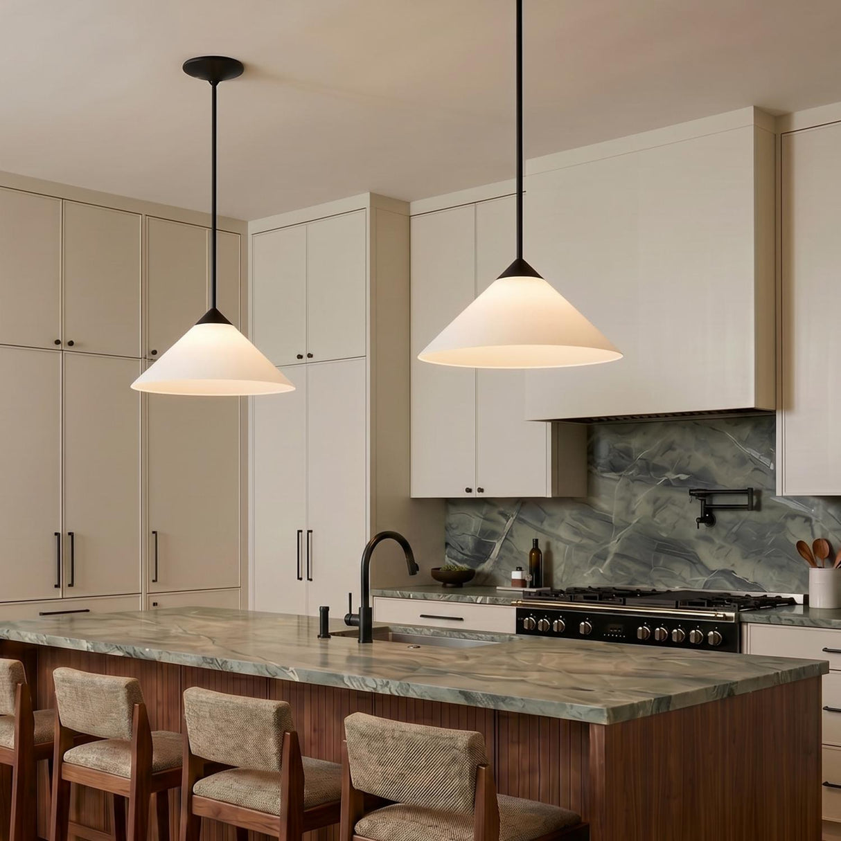 A modern kitchen with two matte black and opal glass cone pendants suspended over a green marble island and beige cabinetry with integrated hardware.