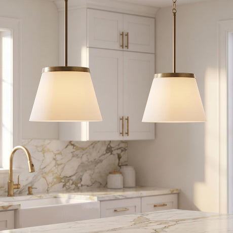 A transitional kitchen with two aged brass and opal glass pendants suspended over a white marble island with white shaker cabinets and a marble backsplash.