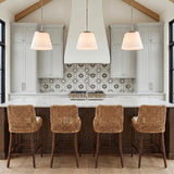 A modern farmhouse kitchen with three brushed nickel and opal glass pendants suspended over a white marble island under a vaulted beamed ceiling with woven stools.
