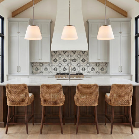 A modern farmhouse kitchen with three brushed nickel and opal glass pendants suspended over a white marble island under a vaulted beamed ceiling with woven stools.