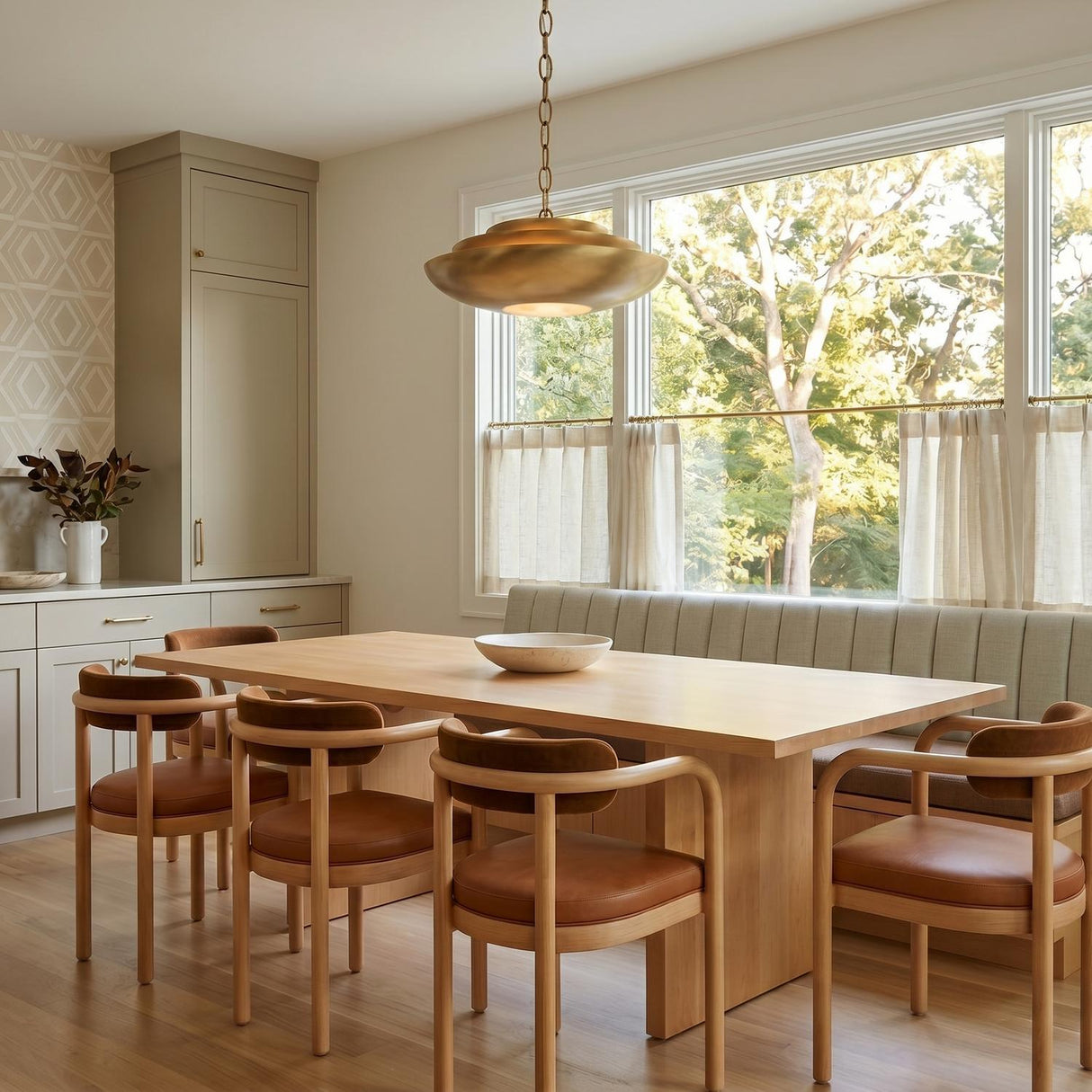 A contemporary dining room with the Calix Large Pendant 22" in aged brass over a light wood dining table and built-in banquette with curved wood chairs.