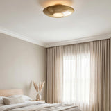 A contemporary bedroom with the Calix Semi-Flush in aged brass and alabaster on the ceiling center above neutral bedding and floor-to-ceiling beige curtains.