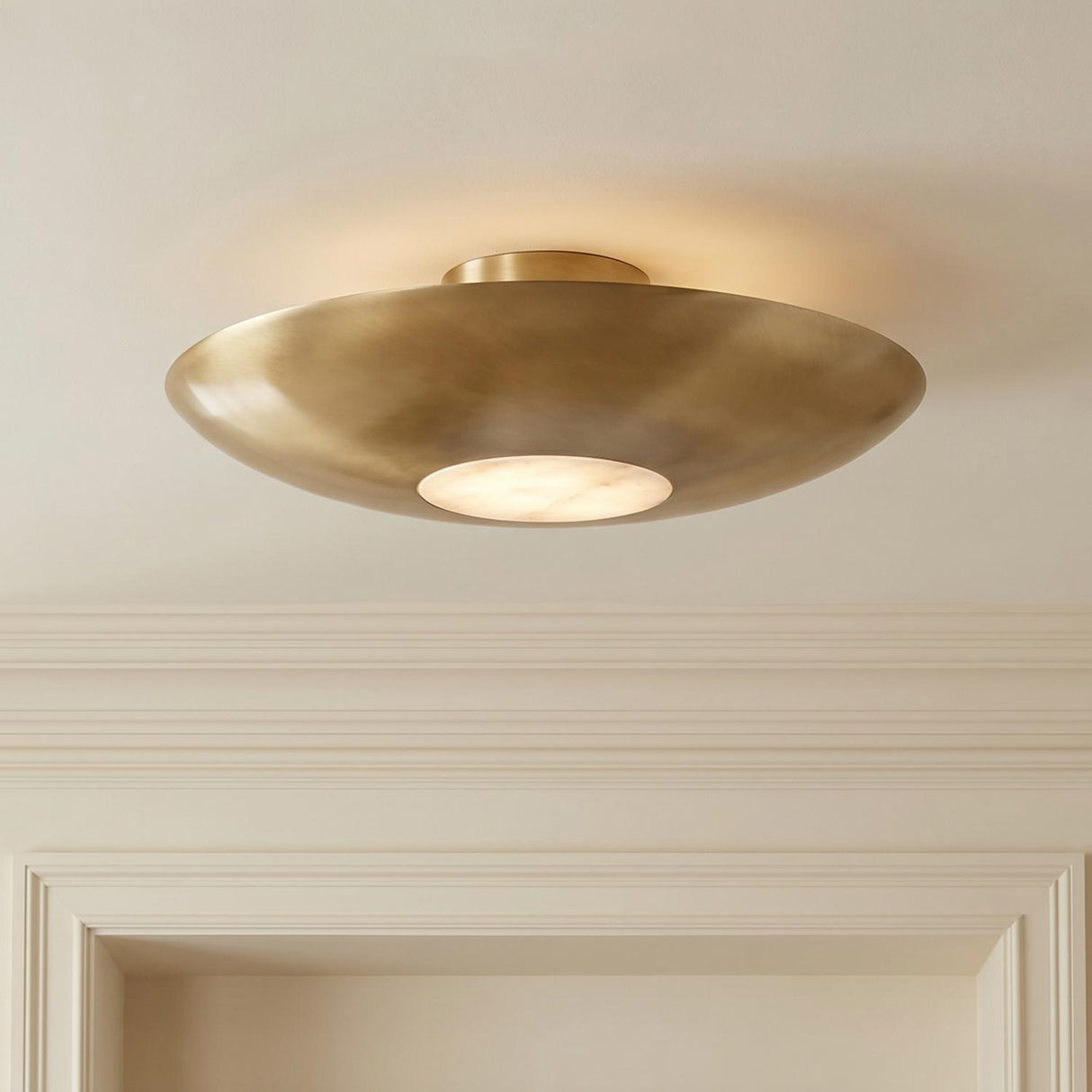 A transitional foyer with an aged brass and alabaster semi-flush mount fixture on a standard ceiling center above traditional cream crown molding and doorways.