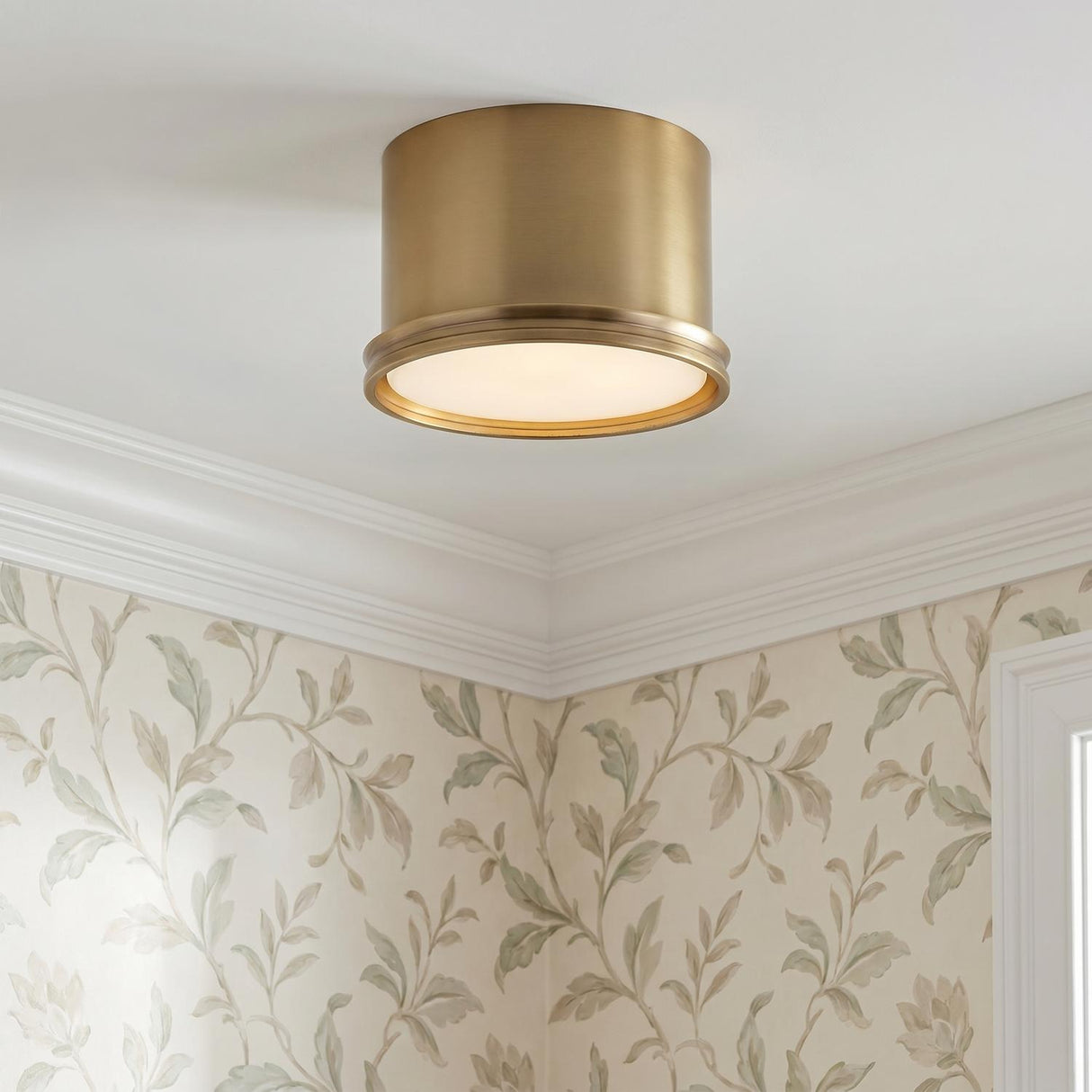 A traditional foyer with the Darrow Small Flush Mount 9 inch Aged Brass fixture mounted on the ceiling above botanical patterned wallpaper and white crown molding.