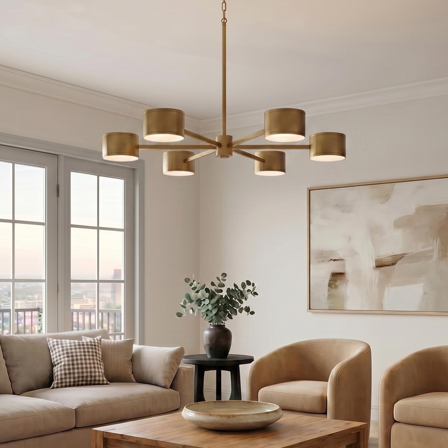 A contemporary living room with the Carmine LED Chandelier in an aged brass finish hanging in the center above a wood coffee table and tan armchairs.