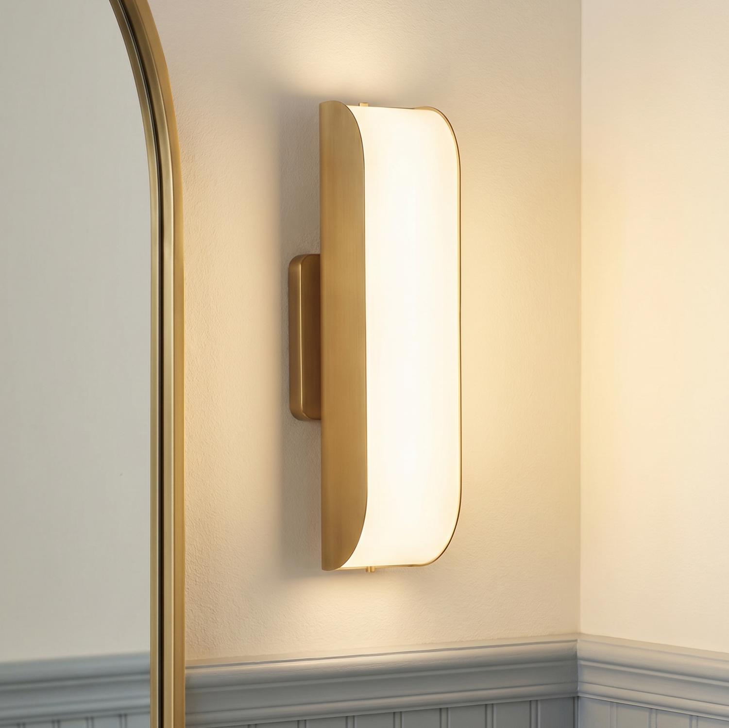A transitional bathroom featuring a Cian LED Wall Sconce in aged brass and milk glass mounted next to an arched gold mirror above blue wainscoting.