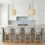 A coastal kitchen featuring two aged brass and ivory rattan pendants over a marble island with light blue cabinetry and a picket tile backsplash.