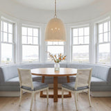 A coastal dining room featuring the Camiri Extra Large Pendant 25", Aged Brass and Ivory Beaded shade over a round wood table with a blue banquette and white cane chairs.