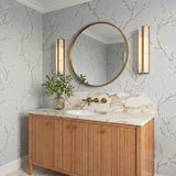 A transitional bathroom with two Azura LED Vanity 24" fixtures in aged brass and alabaster flanking a round mirror above a fluted wood vanity with marble countertops.