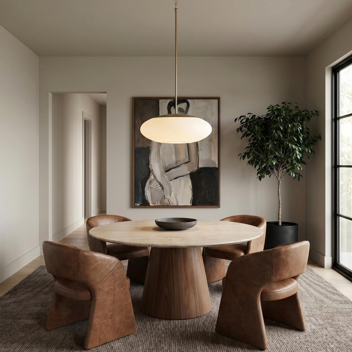 A contemporary dining room featuring an Evora Pendant in aged brass and opal glass hanging over a marble-topped table with a walnut pedestal and leather chairs.