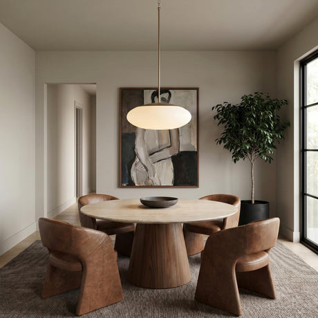 A contemporary dining room featuring an Evora Pendant in aged brass and opal glass hanging over a marble-topped table with a walnut pedestal and leather chairs.