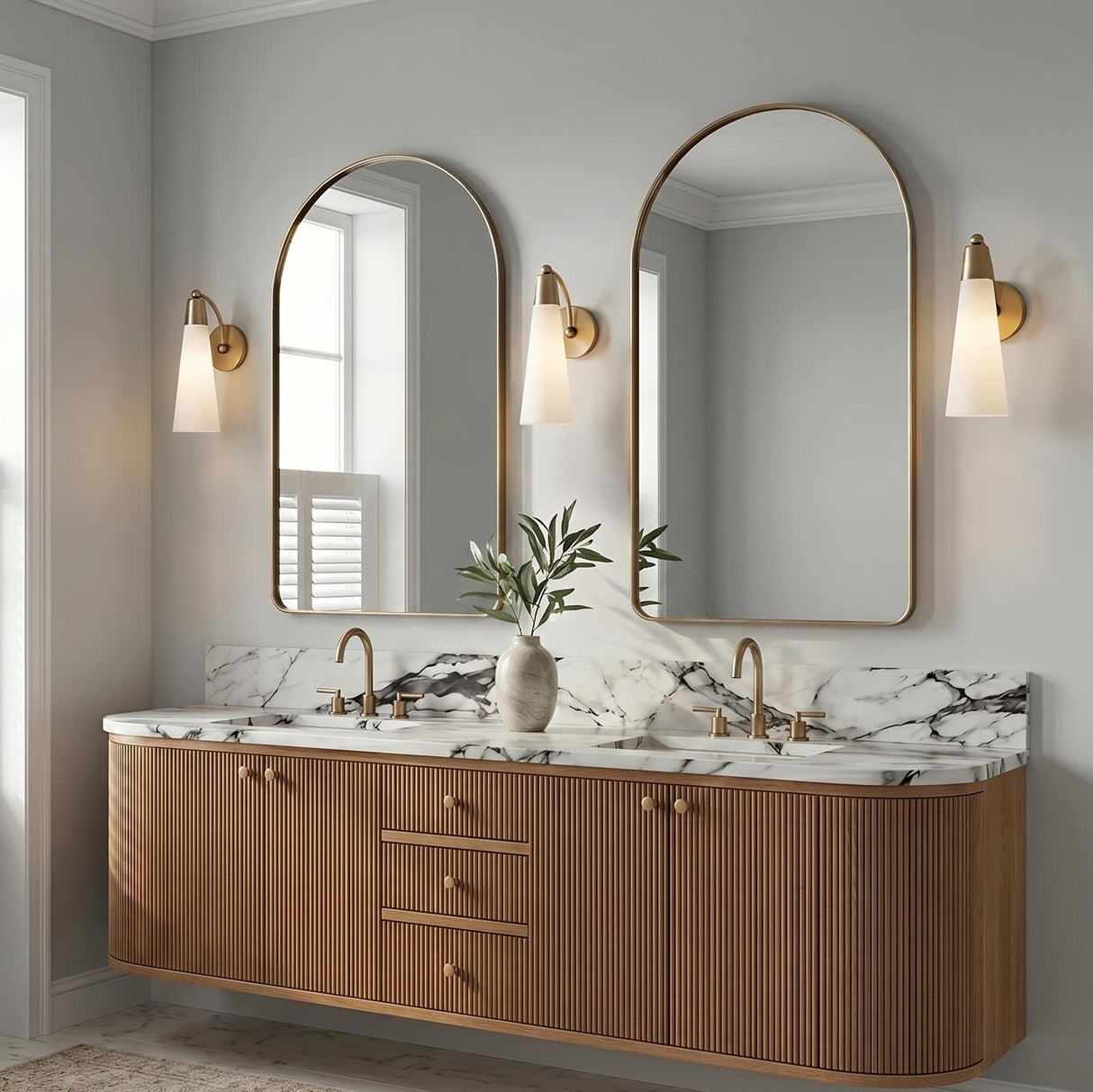 A modern bathroom with three Ethel Wall Sconce fixtures in aged brass and opal glass flanking arched mirrors above a fluted wood vanity with marble countertops.
