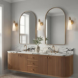 A modern bathroom with three Ethel Wall Sconce fixtures in aged brass and opal glass flanking arched mirrors above a fluted wood vanity with marble countertops.