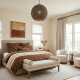 A transitional bedroom featuring the Esmara Pendant 24", Gray Wash Wooden Beads and Dark Matte Brass along the ceiling center over a cream bed with brown patterned linens.