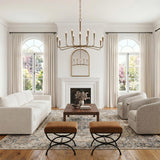 A transitional living room featuring the Myra 12 Light Chandelier in artisan brass hanging over a walnut coffee table near a white fireplace and arched windows.