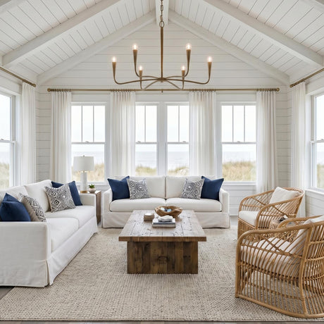 A coastal living room with the Myra 6 Light Chandelier 39", Artisan Brass centered under a vaulted shiplap ceiling above white slipcovered sofas and woven rattan chairs.
