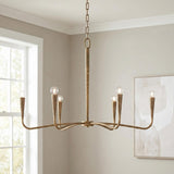 A transitional living room featuring the Myra 6 Light Chandelier 39", Artisan Brass in a textured finish suspended from the ceiling center near a large white-trimmed window.
