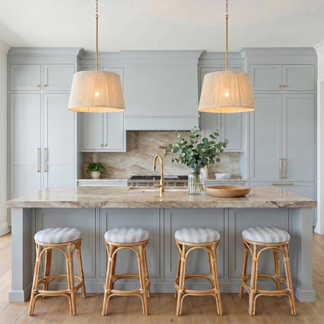 A coastal kitchen with two Malou Conical Pendants in natural rope and matte brass over a beige marble island with pale blue cabinetry and rattan stools.