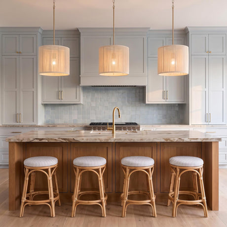A coastal kitchen with three Malou Drum Pendants in natural rope and matte brass suspended over a marble-topped wood island with four woven barstools.