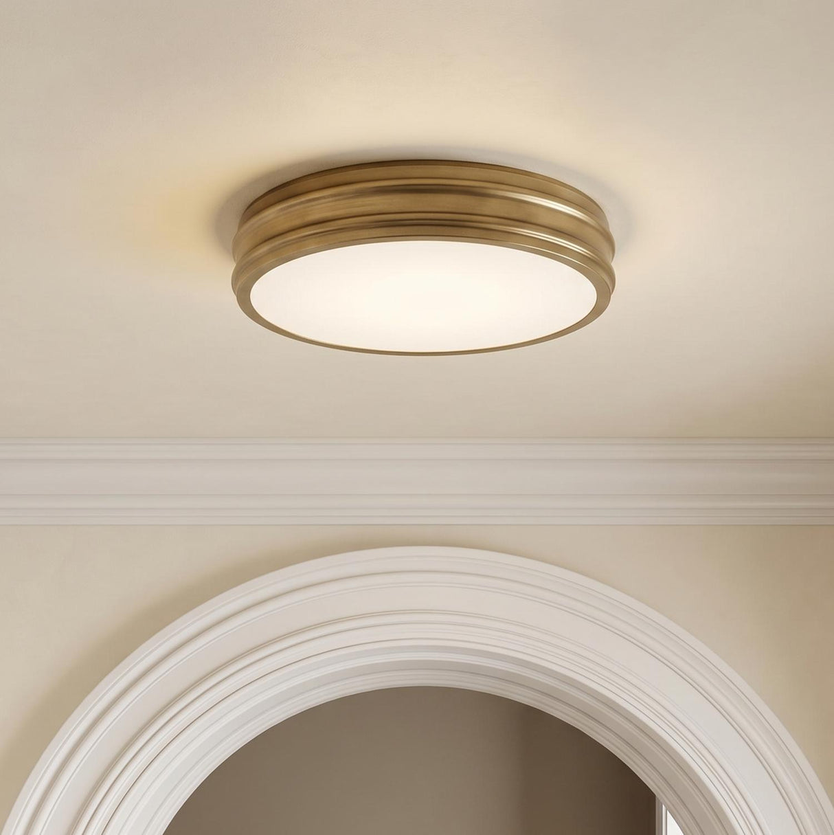 A transitional foyer with the Vanessa LED Flush Mount 16", Aged Brass centered on the ceiling above a white architectural arched doorway and crown molding.