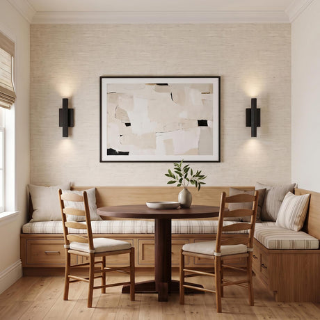 A contemporary dining room with two Simeon Medium LED Wall Sconces in matte black flanking abstract art above a light wood bench and pedestal table.