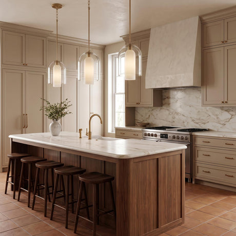 A transitional kitchen with three aged brass pendants featuring clear glass and alabaster diffusers hanging over a walnut island with marble countertops and taupe cabinets.