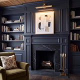 A transitional living room with the Sterling LED Picture Light 22 inch in matte brass mounted above an abstract painting and a black marble fireplace.