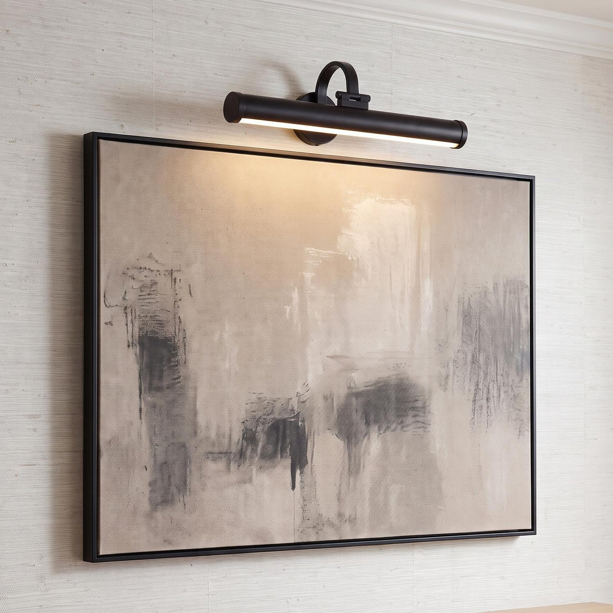 A transitional living room with a Sterling LED Picture Light 22" in matte black mounted over abstract art on a beige textured wall with crown molding.