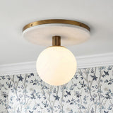 A transitional bedroom with the Araceli Medium LED Semi-Flush 12", Antique Brass and White Marble fixture along the ceiling above blue floral wallpaper and crown molding.