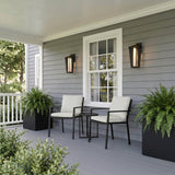 A modern farmhouse porch with two matte black and brass Reynard LED Outdoor Wall Lights glowing on gray siding, flanking a window beside potted ferns.