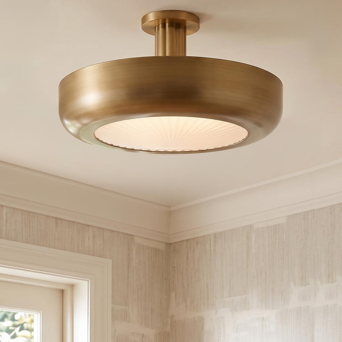 A transitional foyer with an Imara Large LED Semi-Flush in antique brass featuring ribbed glass over textured cream wallpaper and white crown molding.