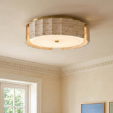 A contemporary living room with the Damari Medium LED Flush Mount in travertine and brass on the ceiling beside white crown molding and framed colorful artwork.