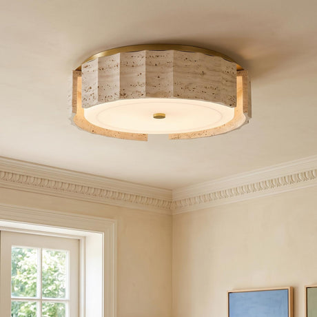 A contemporary living room with the Damari Medium LED Flush Mount in travertine and brass on the ceiling beside white crown molding and framed colorful artwork.