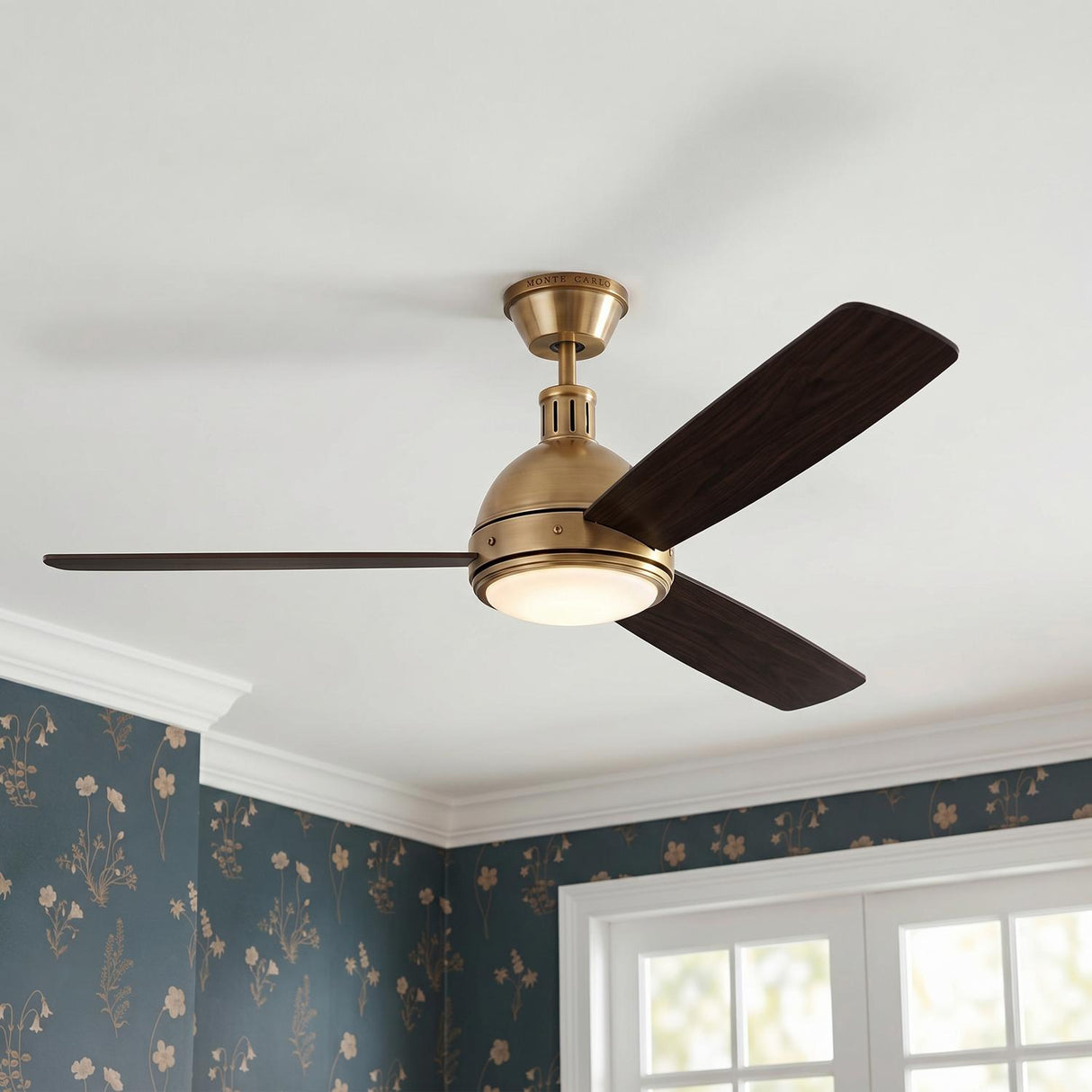 A traditional bedroom featuring the Brant LED Ceiling Fan 60" in antique brass and mahogany wood blades at the ceiling center above blue floral patterned wallpaper.