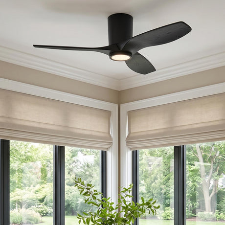 A modern living room featuring the Avocet LED Ceiling Fan 44", Matte Black Oak installed in the ceiling center above large windows with beige Roman shades.