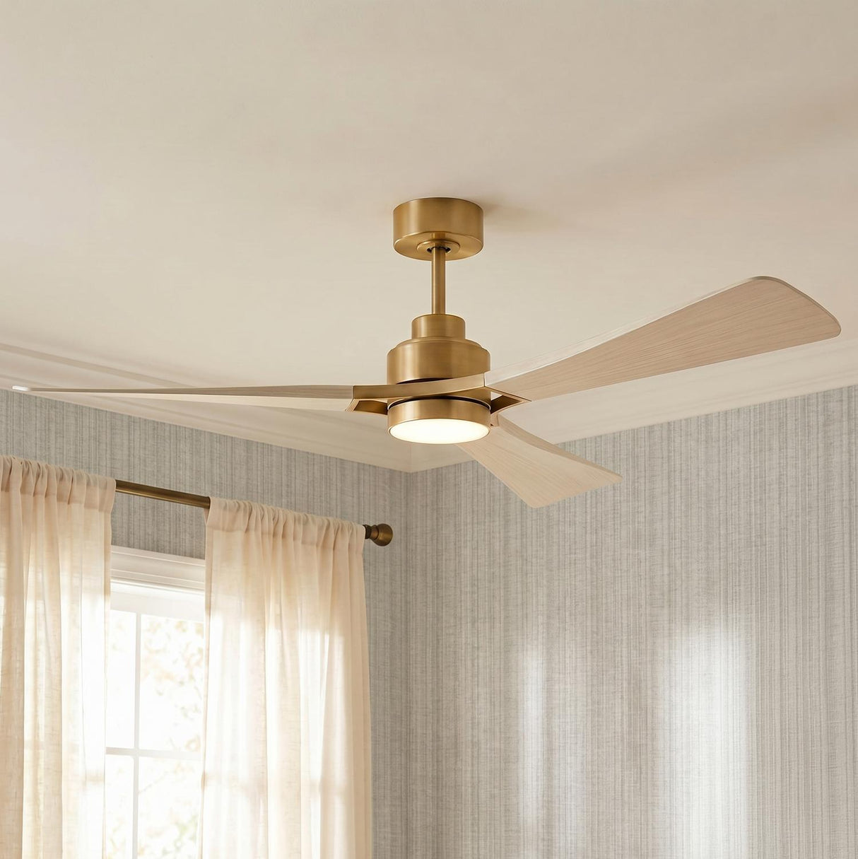 A transitional bedroom featuring the Mallard LED Ceiling Fan 60-inch in modern brass and whitewash oak mounted to the ceiling center near textured gray wallpaper and cream curtains.