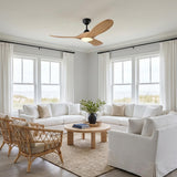 A coastal living room with the Egret LED Ceiling Fan in natural oak and matte black mounted to the ceiling center above white slipcovered sofas and rattan armchairs.