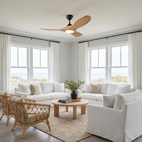 A coastal living room with the Egret LED Ceiling Fan in natural oak and matte black mounted to the ceiling center above white slipcovered sofas and rattan armchairs.